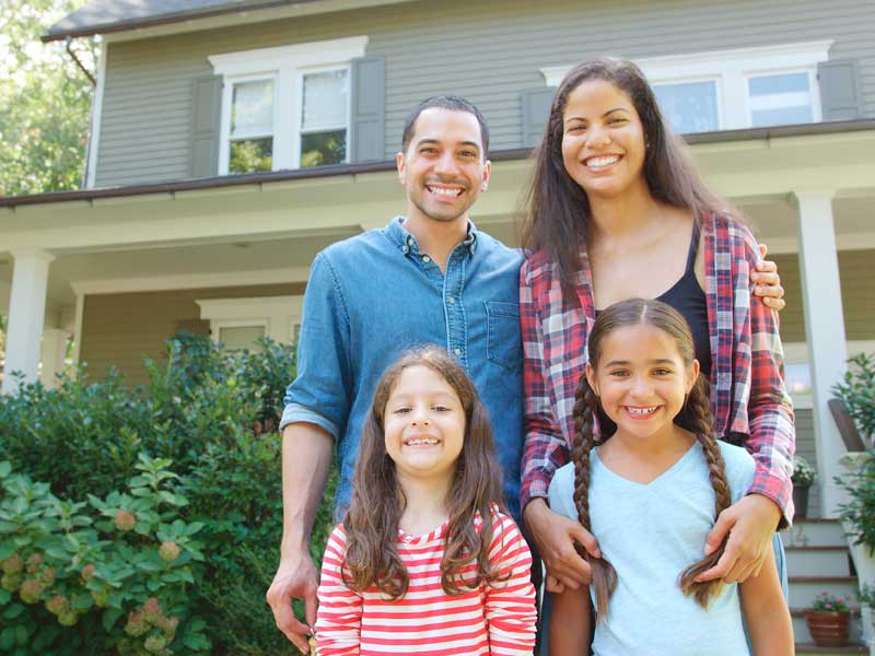 A young family standing outside their home.